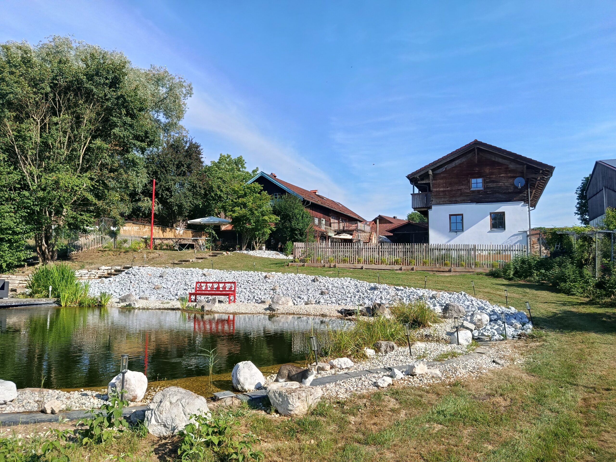 Gepflegte Gartenanlage mit Teich und Bauernhaus im Hintergrund